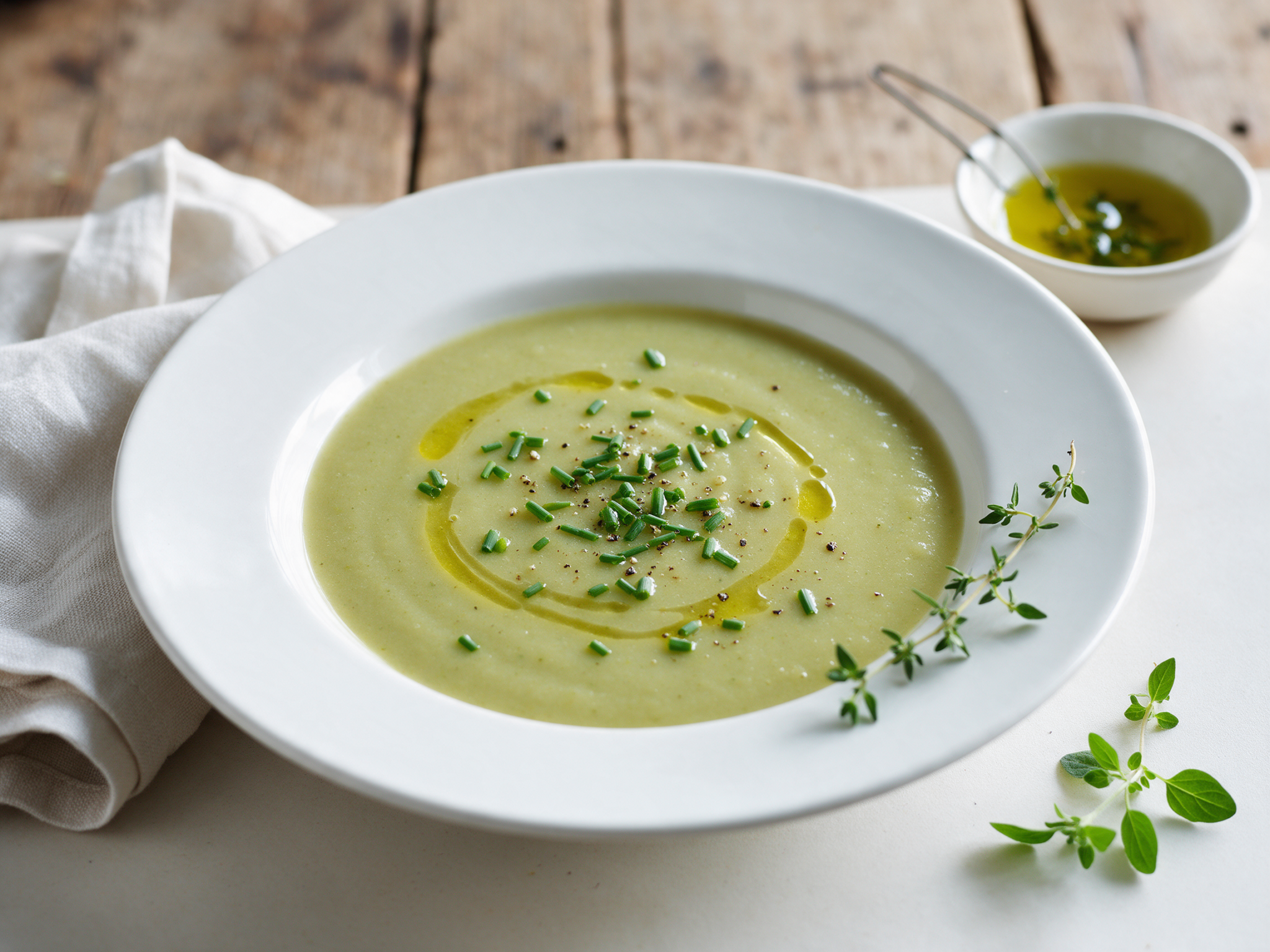 Bowl of pale green roasted leek and potato soup with chives and olive oil on a linen-covered wooden table